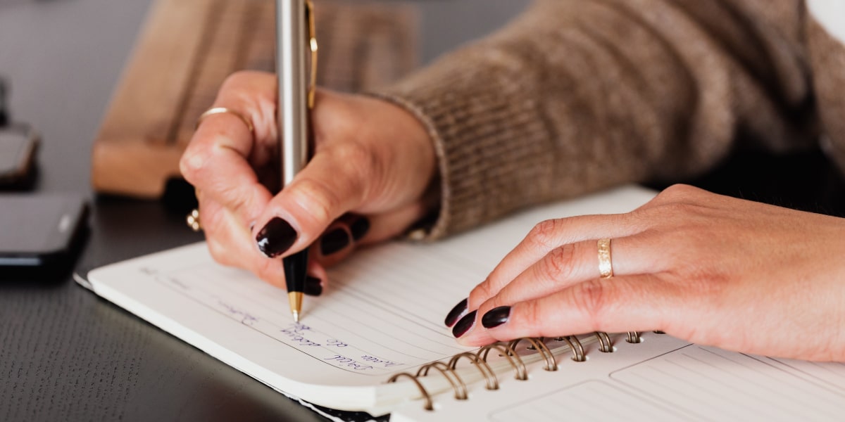 An aspiring UX designer's hands, writing in a planner to organize time for their UX bootcamp