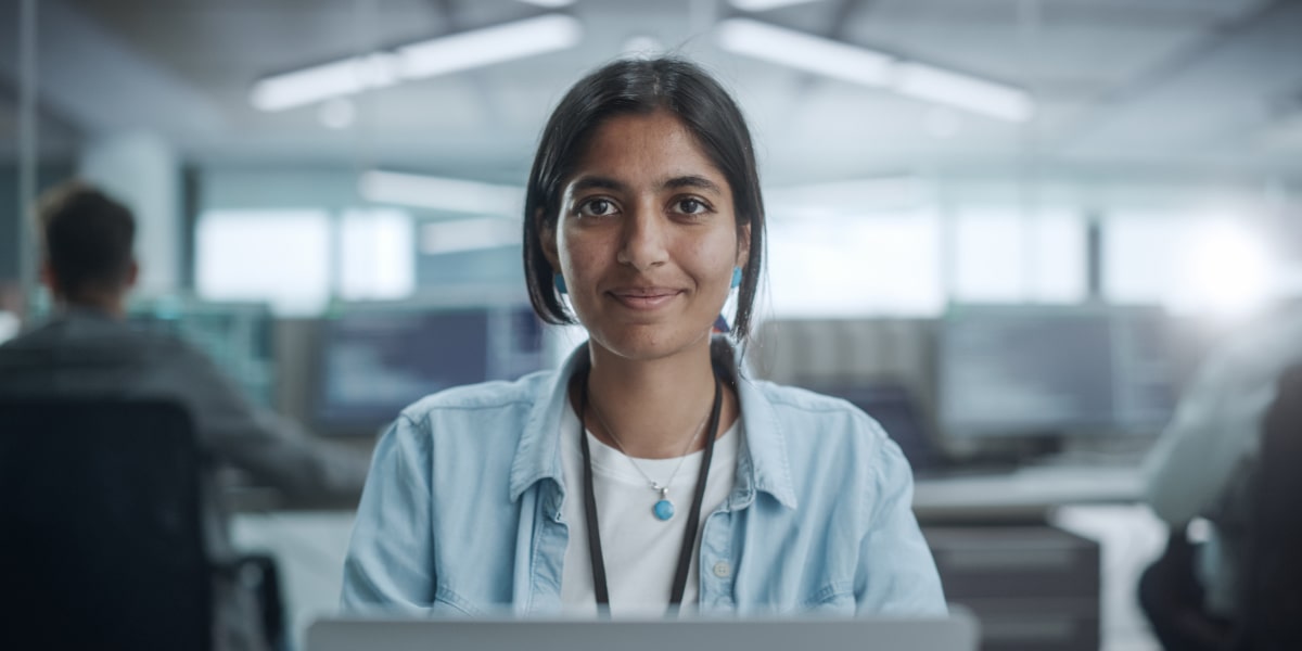 Its not just about what you code but also where you code Female web developer stares at the camera from behind her laptop in a startup office.