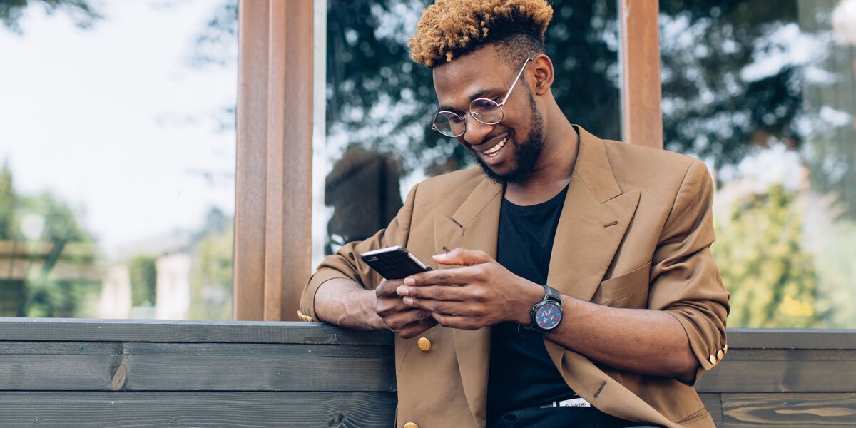 A person sitting on a bench, scrolling on their smartphone, smiling