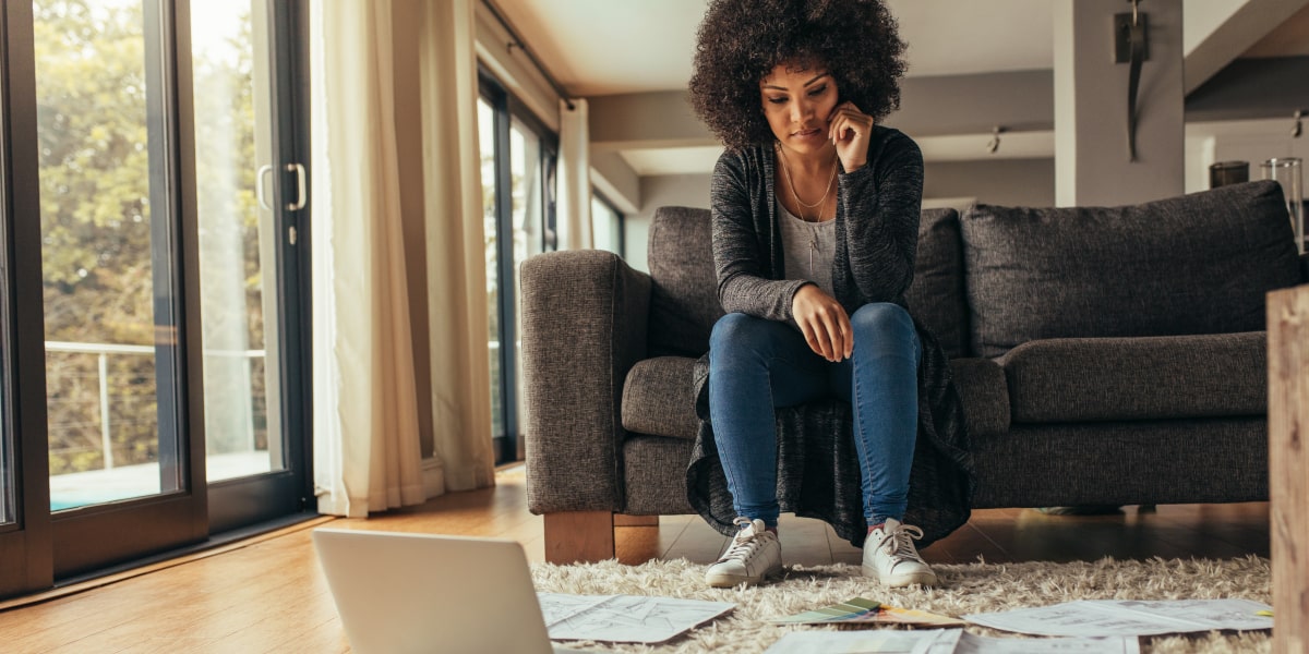 A UI designer sitting on a sofa, with different paper designs spread out over a rug