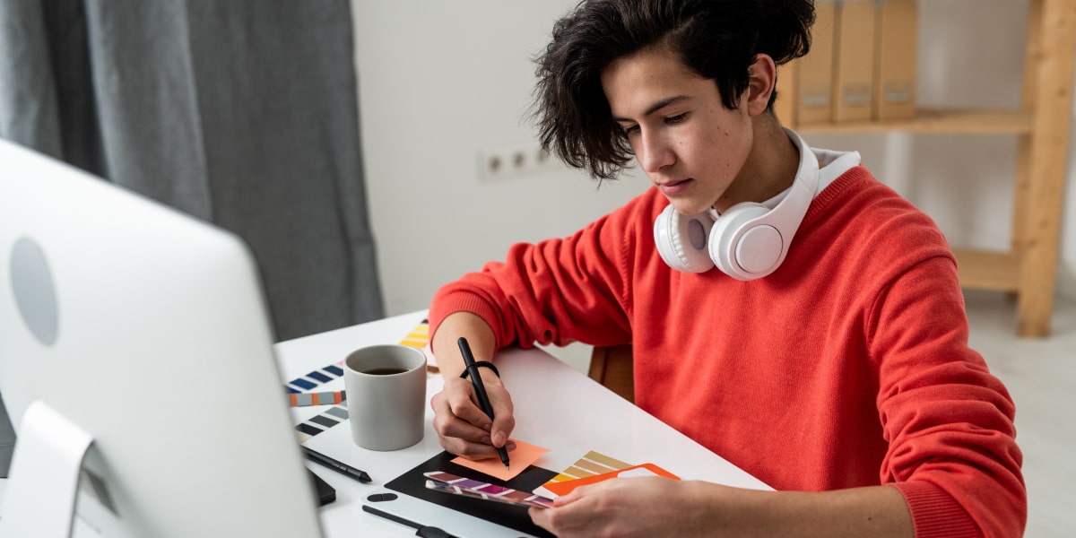 An aspiring UI designer looking at color swatches, sitting at a desk in front of a computer