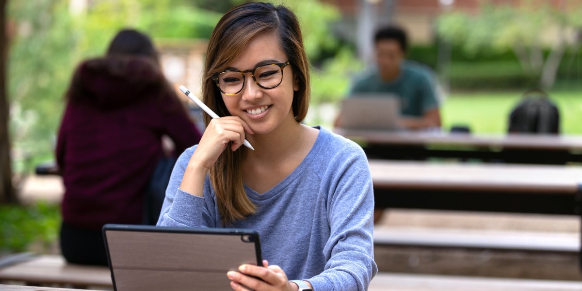 An aspiring digital marketing manager sitting at a wooden bench outside, working on a laptop