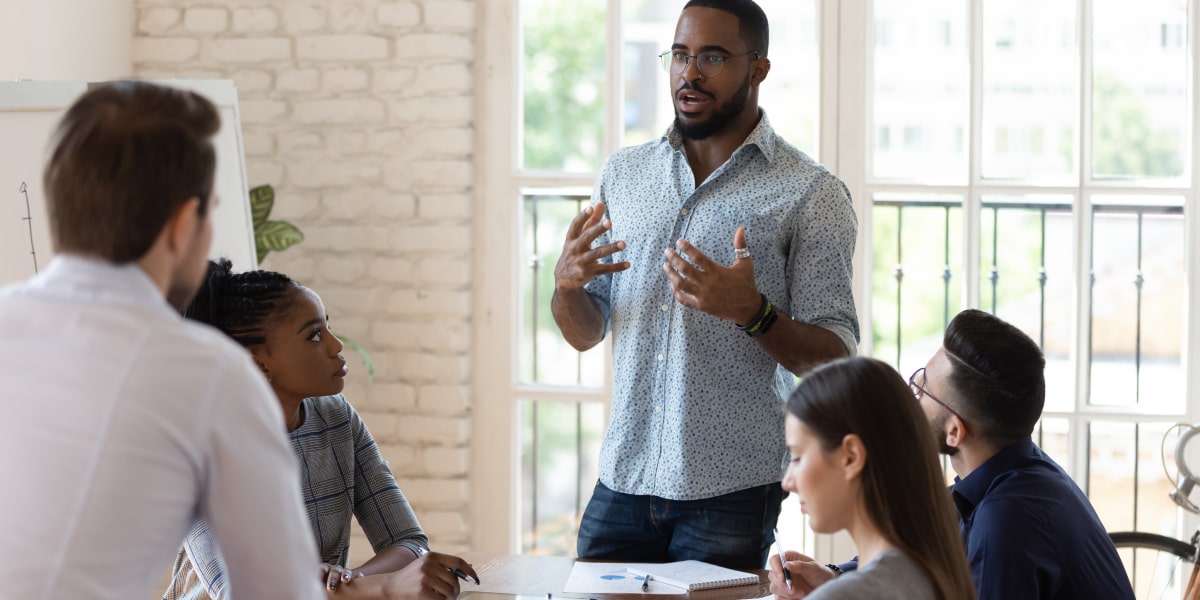 A digital marketing analyst standing in a modern office, giving a presentation to a group of colleagues