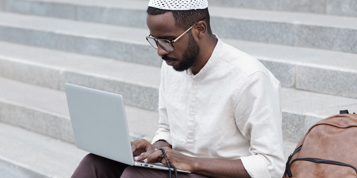 A digital marketing manager sitting on a step outside, working on a laptop