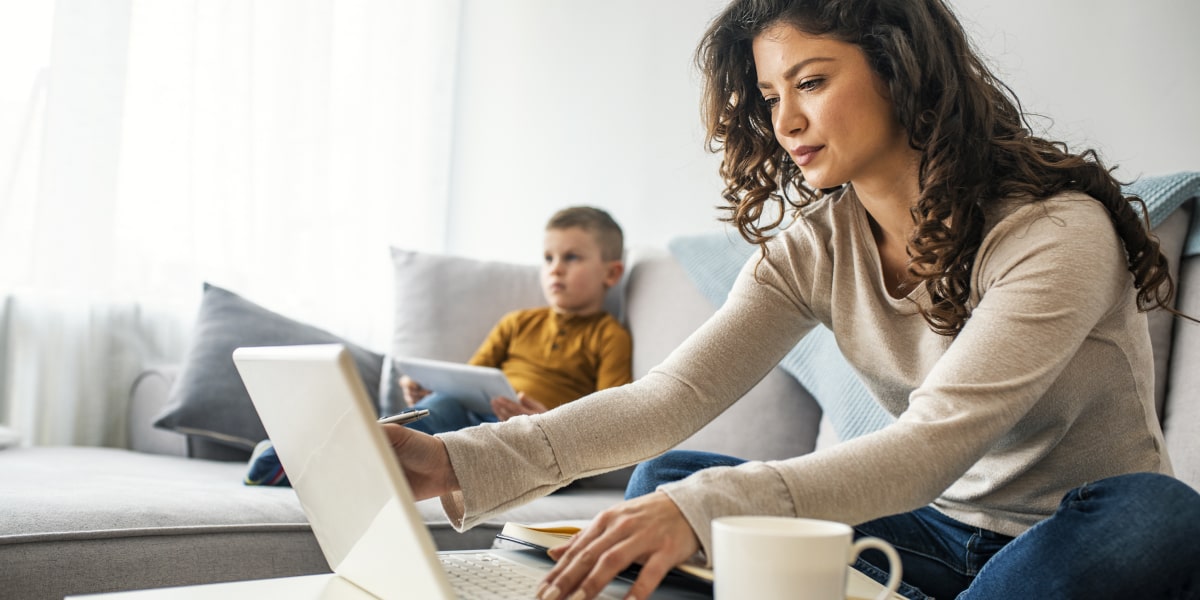 A person working from home, sitting on a sofa with a young child in the background