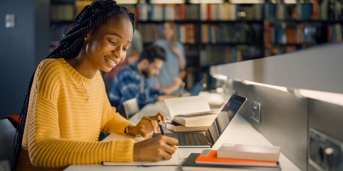 A student sitting at a desk in a library with a laptop, studying for their digital marketing degree