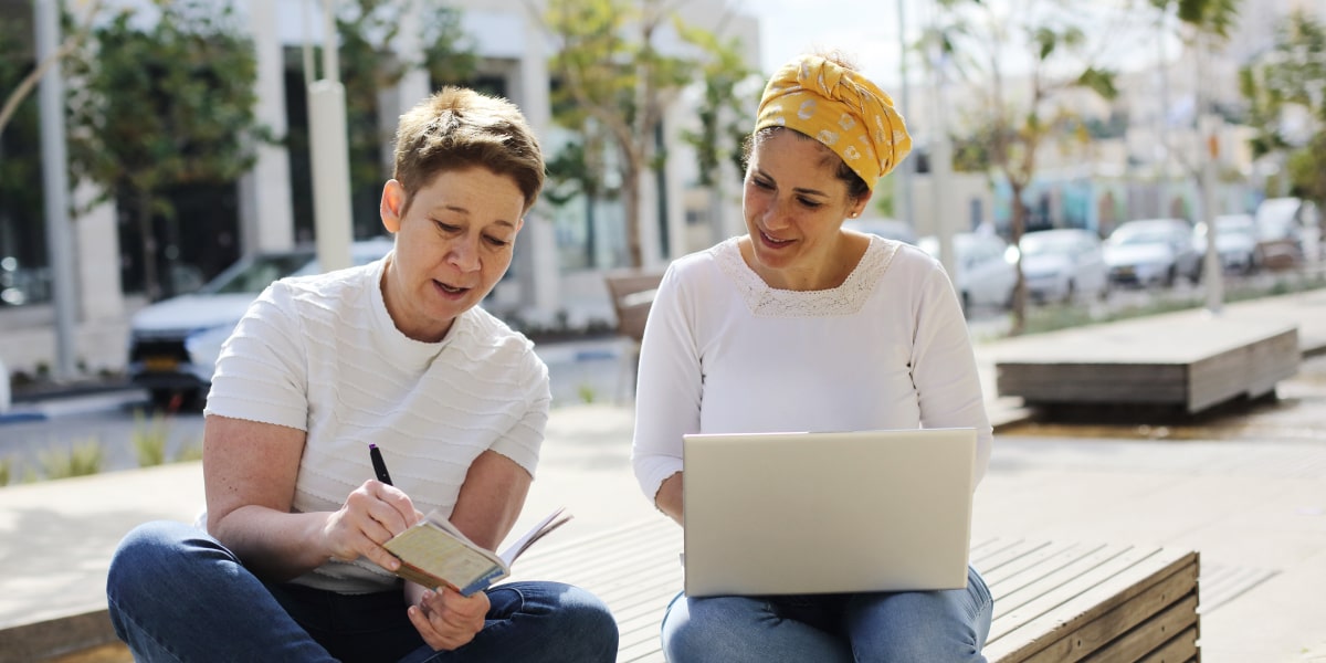 Two designers sitting outside with a laptop, discussing the average animation designer salary