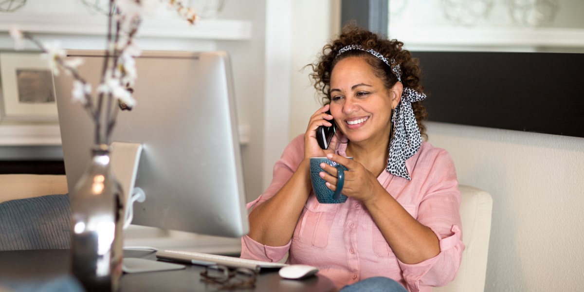 A digital marketing specialist sitting at a desk, speaking on the phone and holding a cup of coffee