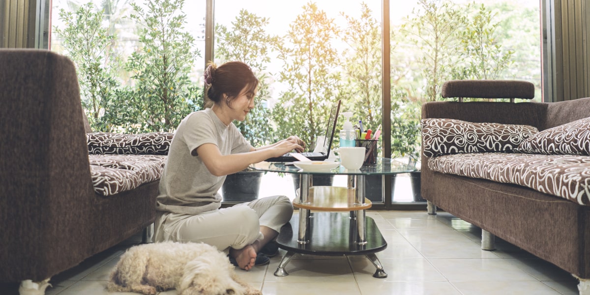 A social media specialist sitting on the floor in side profile, working on a laptop with a dog asleep on the floor next to them