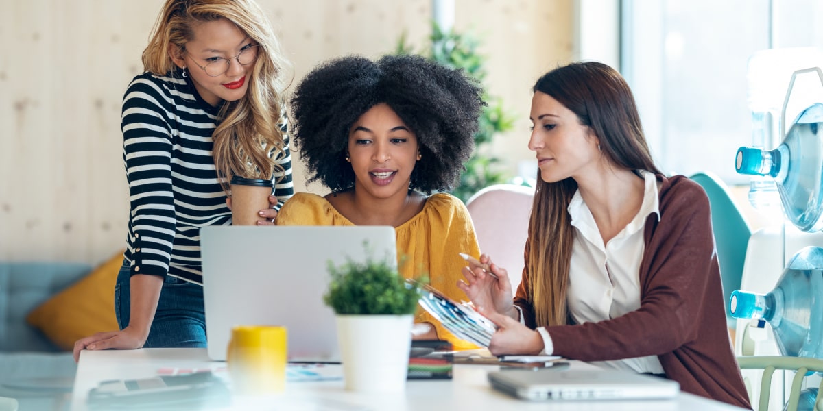 Three marketing professionals in an office, looking at a laptop, researching how to become a social media specialist