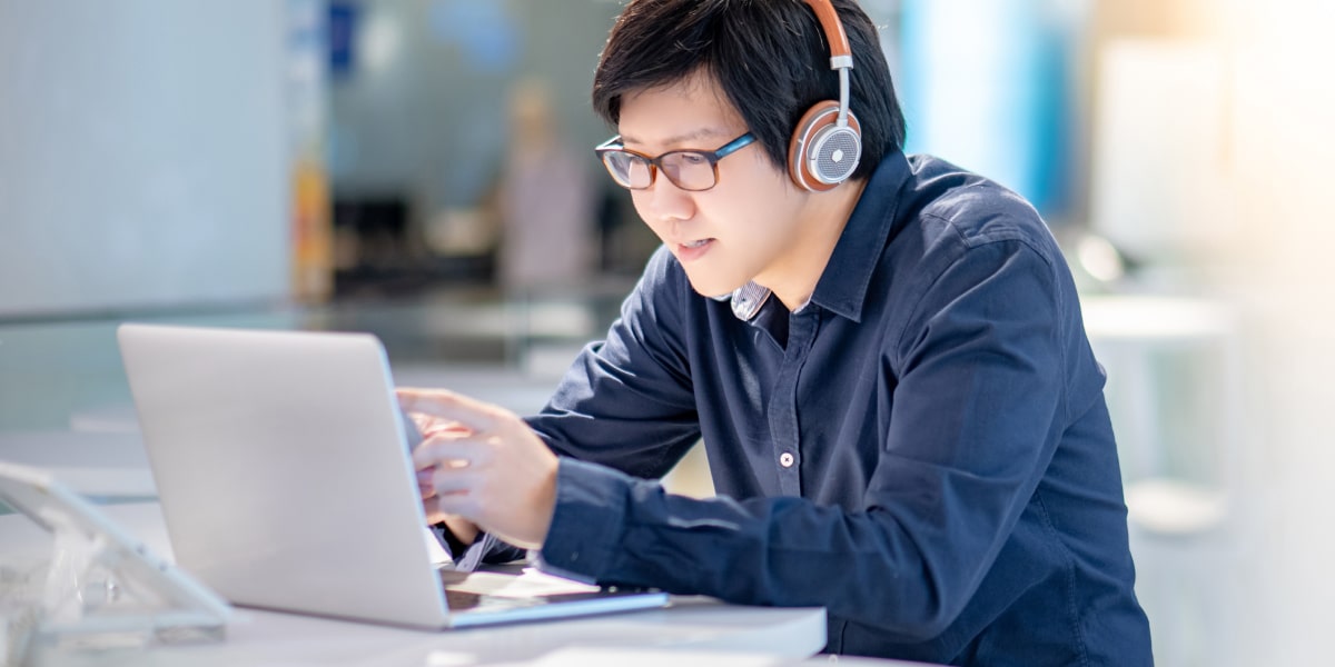 A student on a laptop, wearing headphones, researching how to become a social media manager