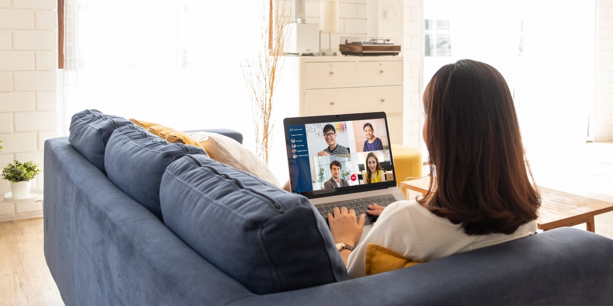 A digital marketing manager sitting on a sofa, having a video call on a laptop with other digital marketing professionals