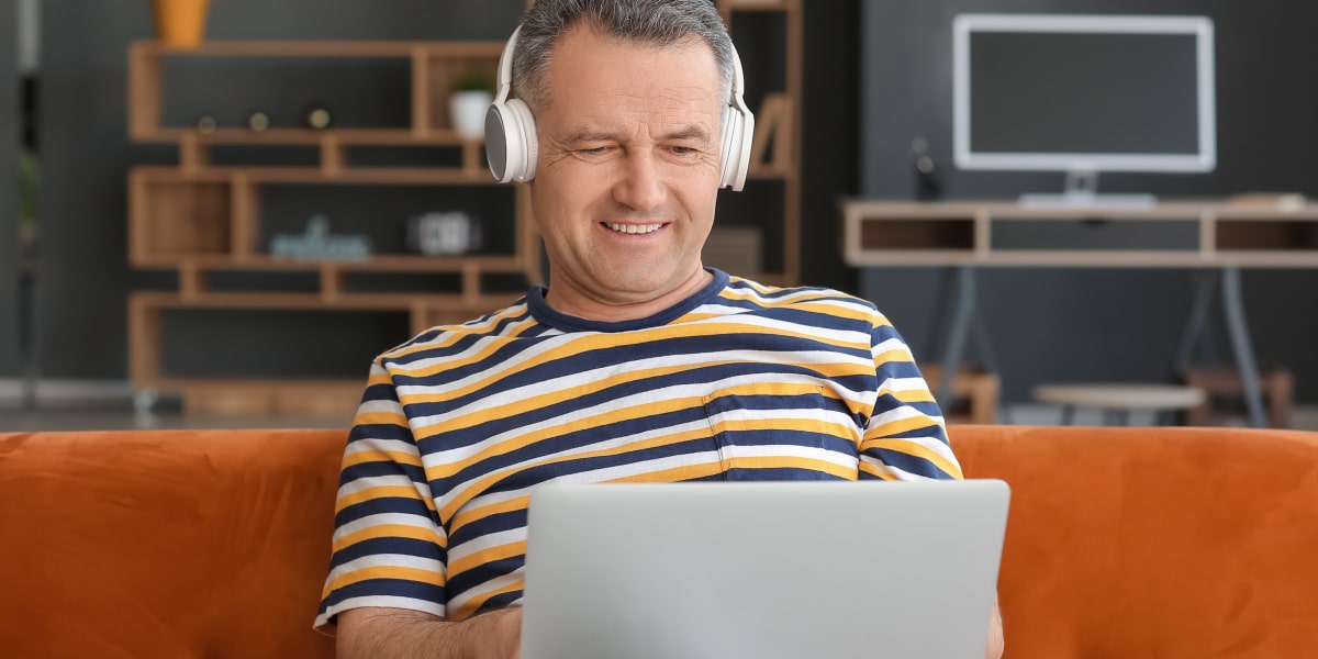 A digital marketing degree student sitting on a sofa, wearing headphones, working on a laptop