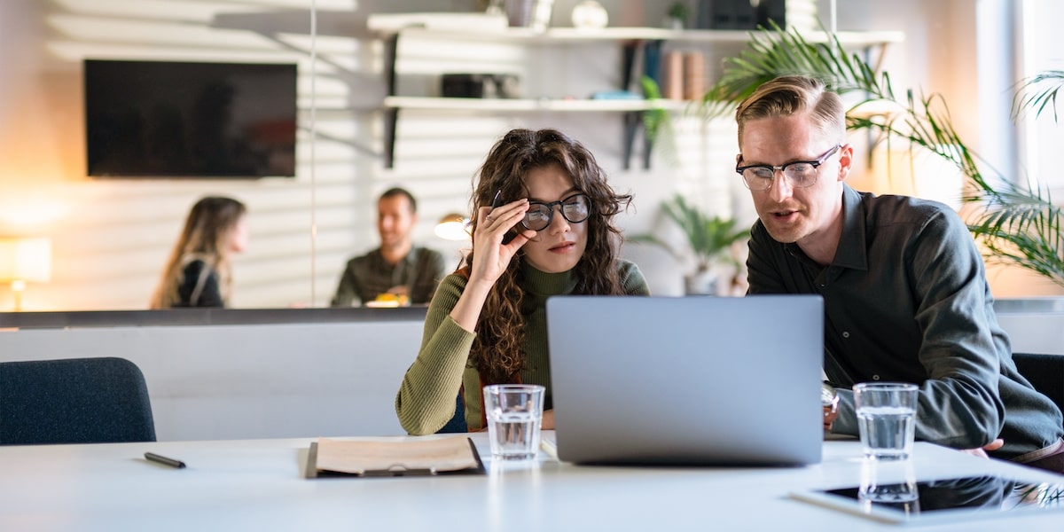 A cloud engineer explains something to a product manager on a laptop in an office.