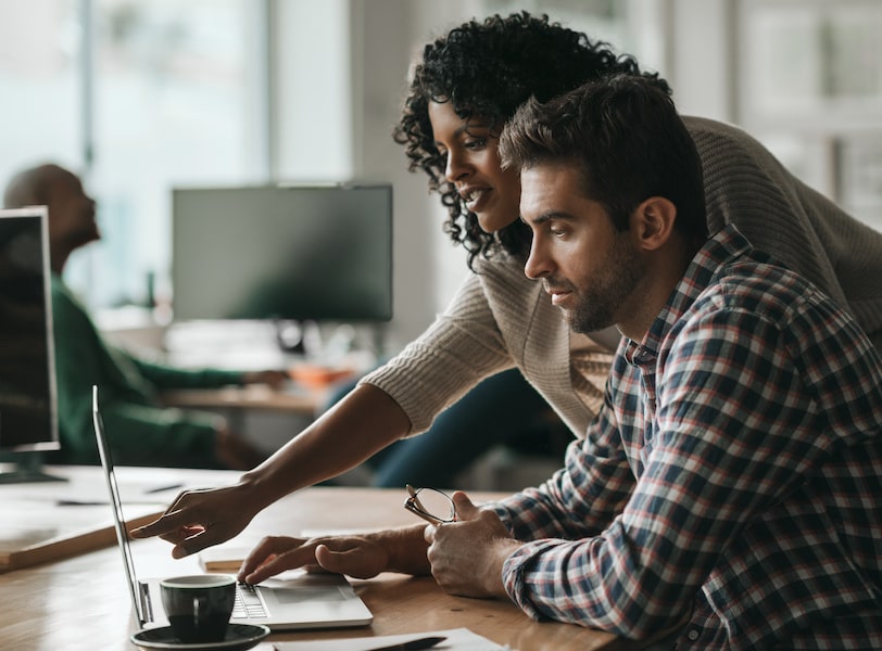 A product manager explains a product roadmap to a designer on a desktop computer.