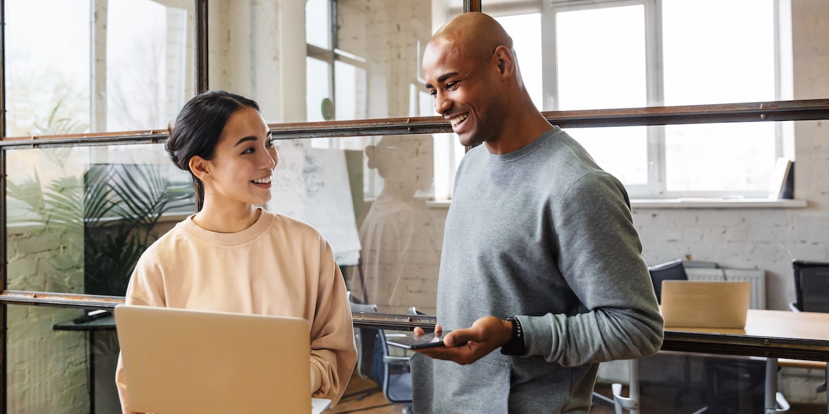 A web developer shows a tech stack to her colleague on a laptop in a bright office.