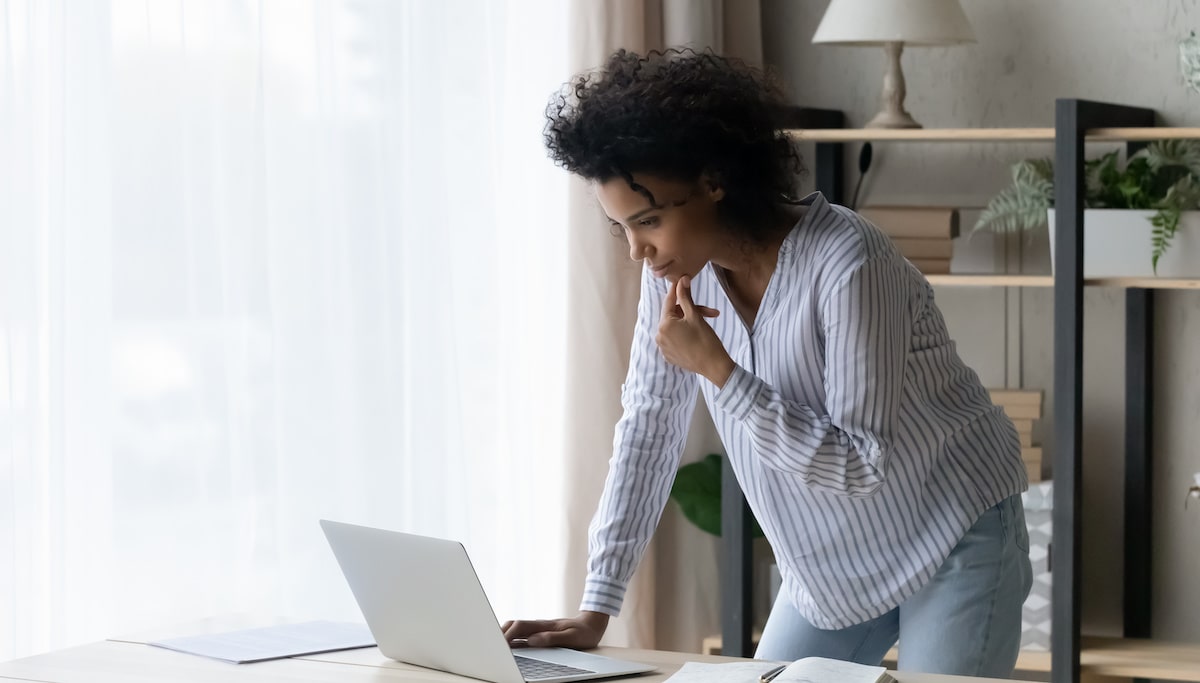 A product manager stands in her home office looking at her laptop studying Scrum processes.