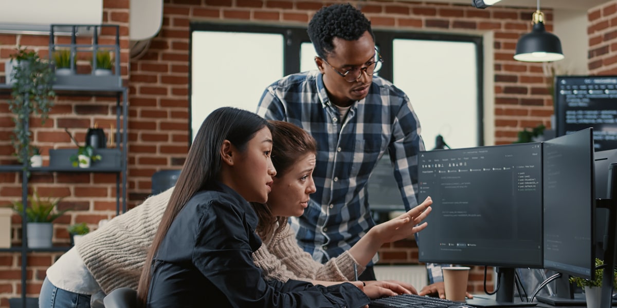 Three developers in an office discuss some code on a computer screen.