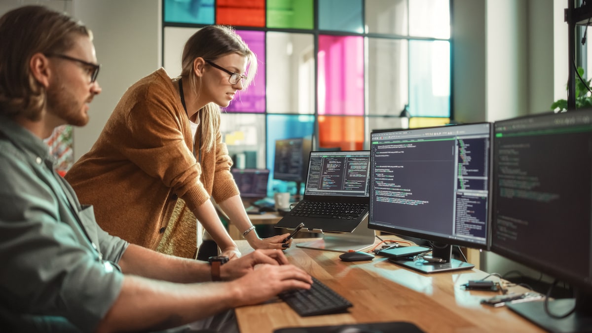 A developer teaches her colleague what is debugging in a bright startup office.