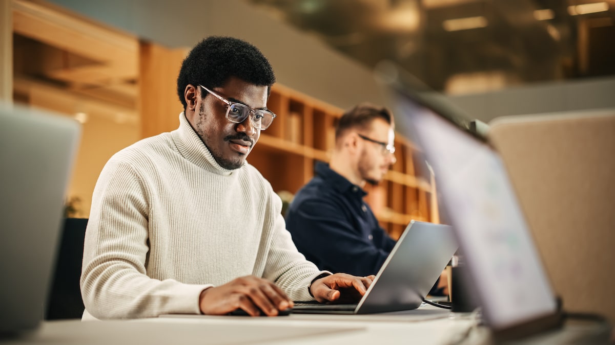 A technical product manager sits at his computer in a workspace analyzing data.