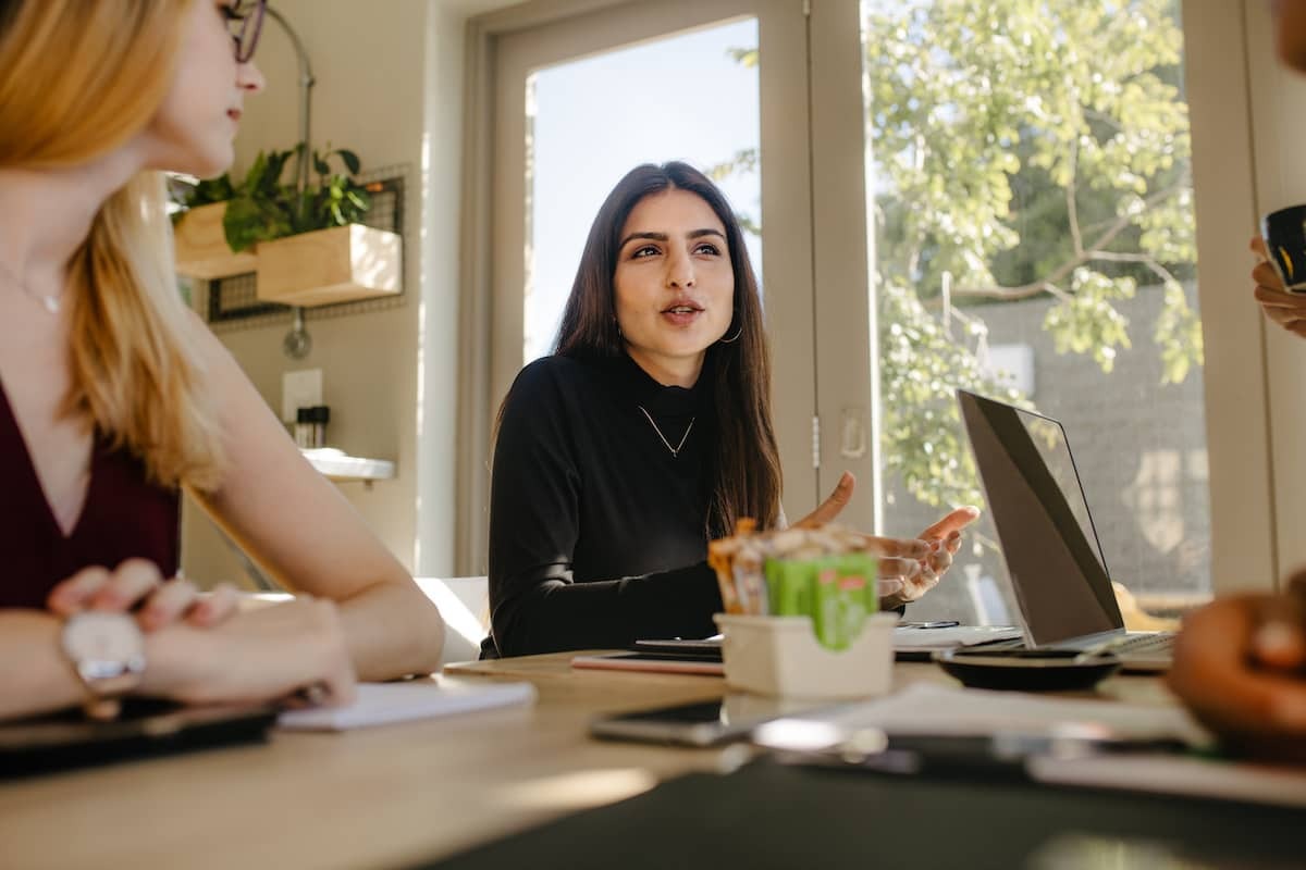 A product designer in a meeting sat at a table with laptop talking with other designers