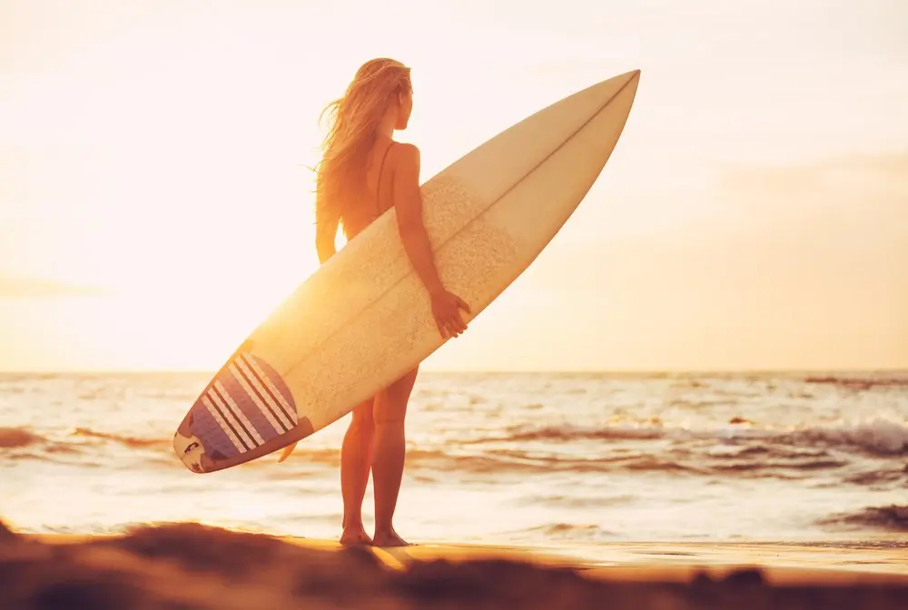 A woman holding a surfboard on a beach at sunset