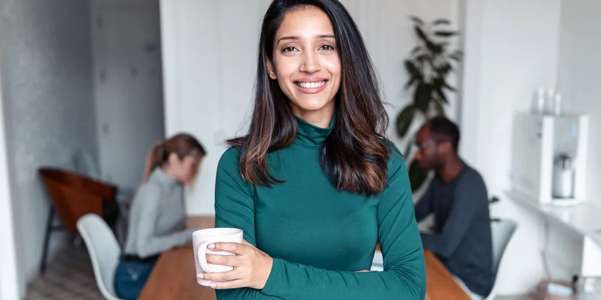 A data analyst holding a cup of coffee, smiling