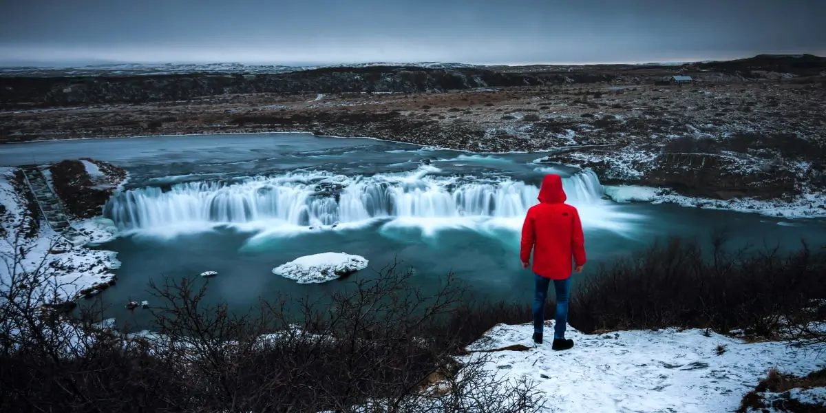 Shot of a person in a red coat standing by a waterfall showing the rule of thirds.