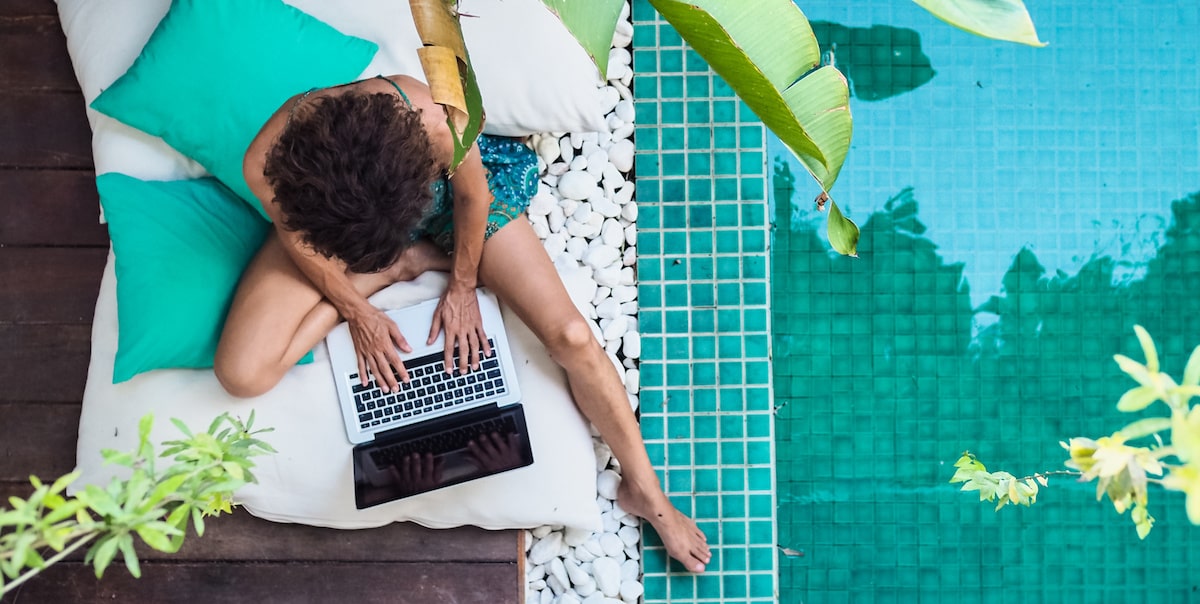 Woman doing remote jobs on a laptop at a tropical pool