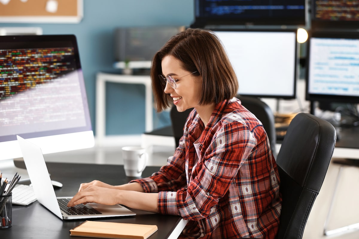 A female programmer works away at a computer surrounded by screens of code.