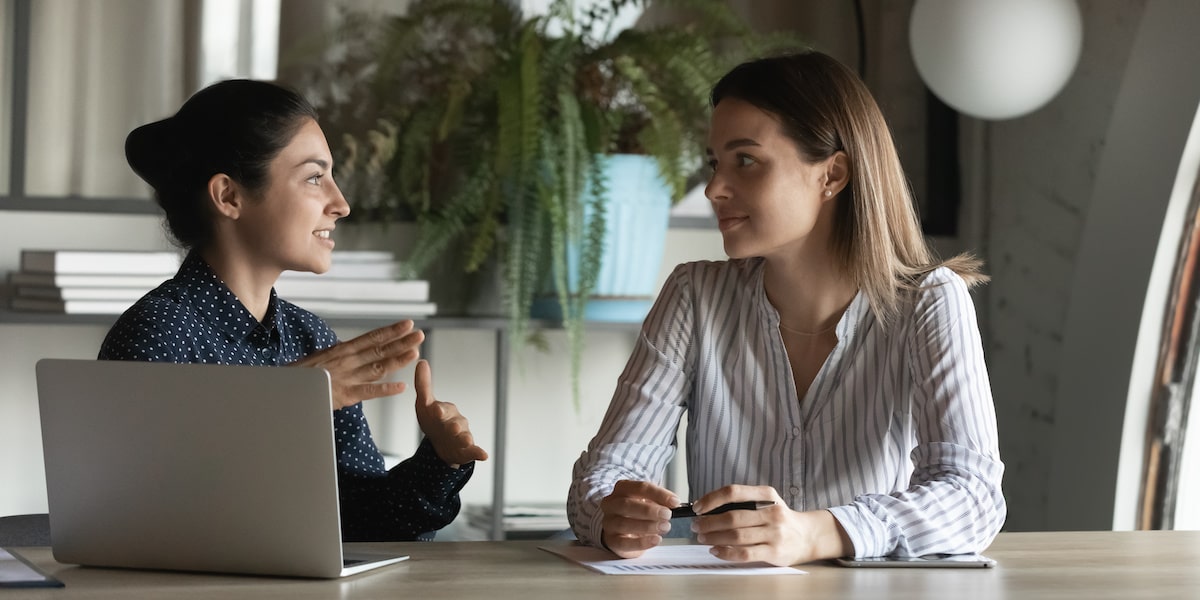 A software engineer and growth product manager talk to each other beside a laptop.