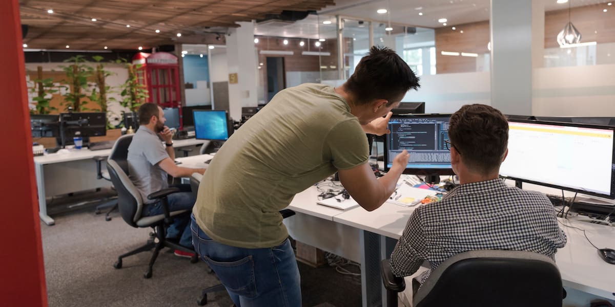 Two men working machine learning jobs discuss data on a computer screen.