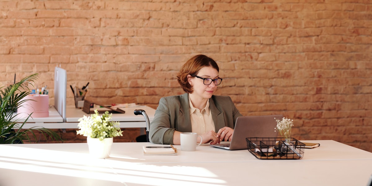 Female web developer sits in a wheelchair working on a laptop in an office