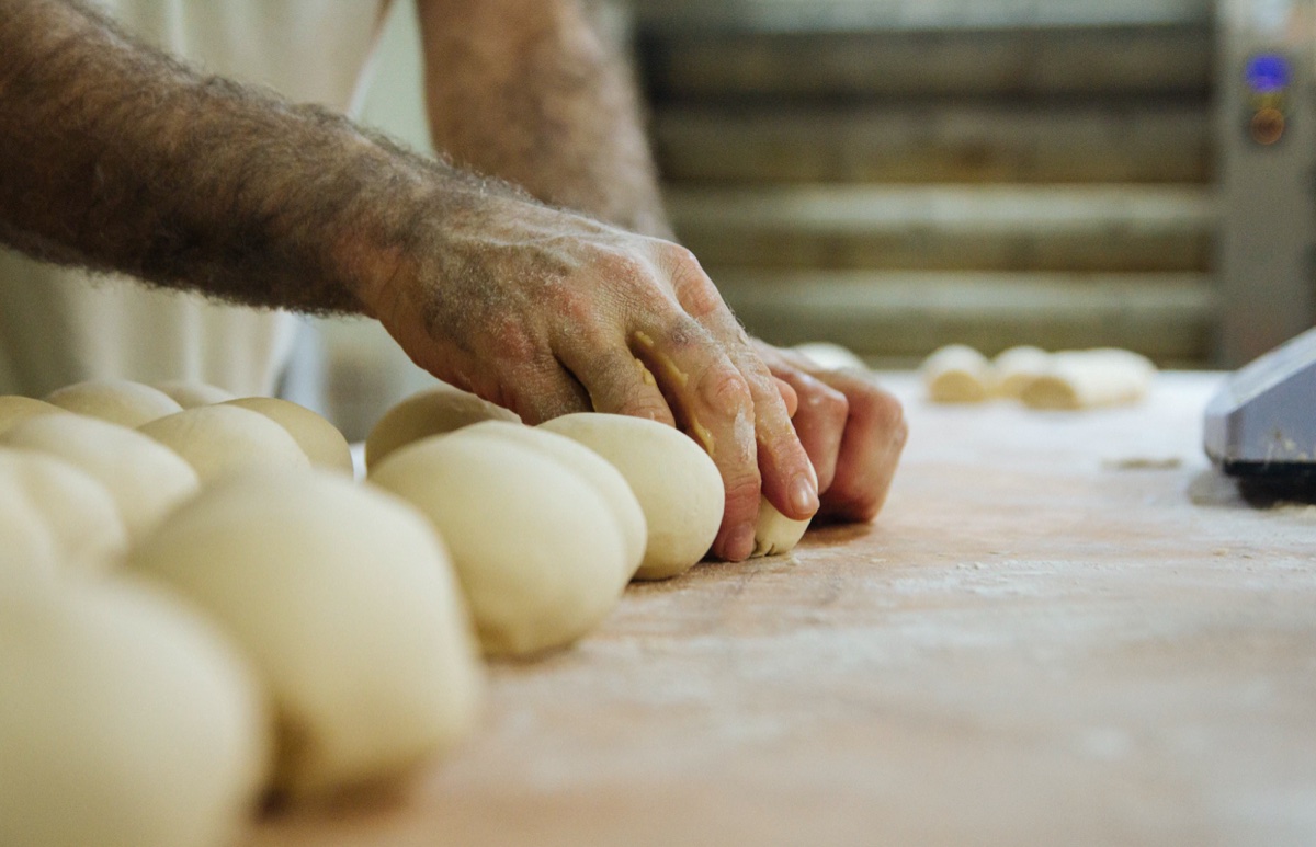 Baker's hands shaping rounds of bread dough .