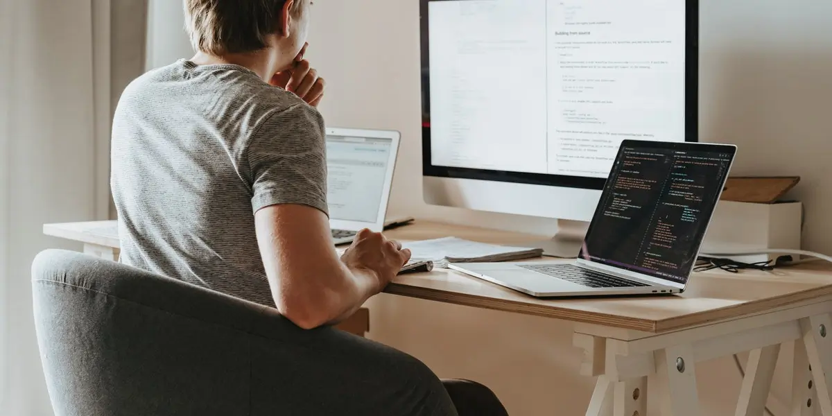 Man sits at a desk with two laptops and a monitor to learn to code
