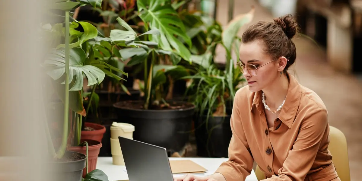 A UX designer works at her laptop in a leafy cafe.