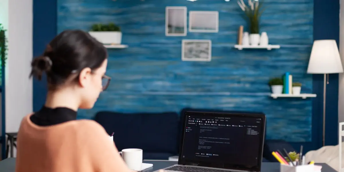 JavaScript is known as one of the three pillars of the internet Female JavaScript developer sits at a desk in a startup office, coding on a laptop.