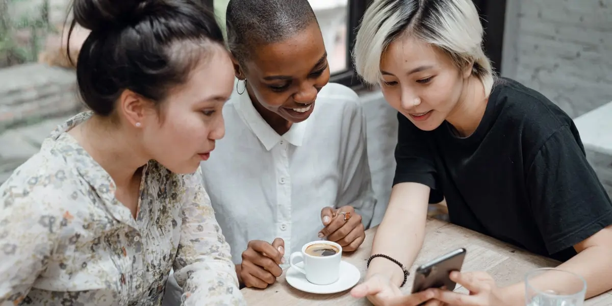 careerpath uxdesign firstjob min Three UX designers gathered at a table, looking at recent project results on a phone