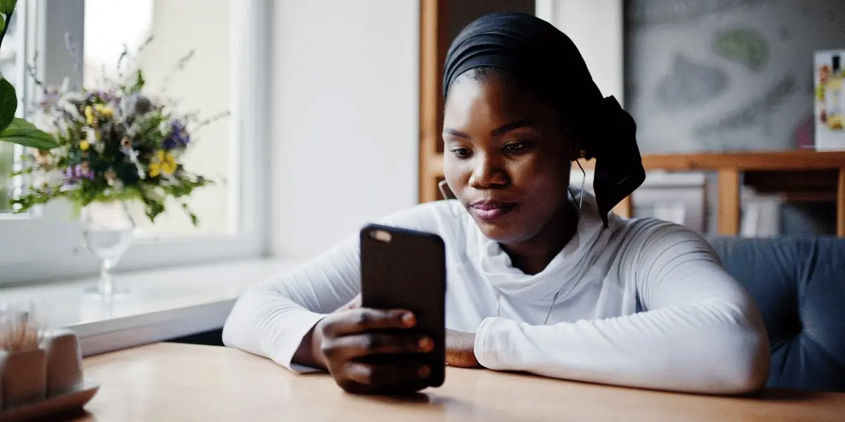 A person sitting at a table near a window, working on a mobile phone.
