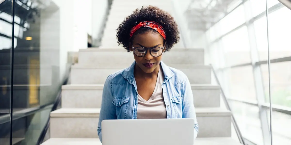 A woman sitting on the stairs with her laptop researching the best web development tutorials on the internet.
