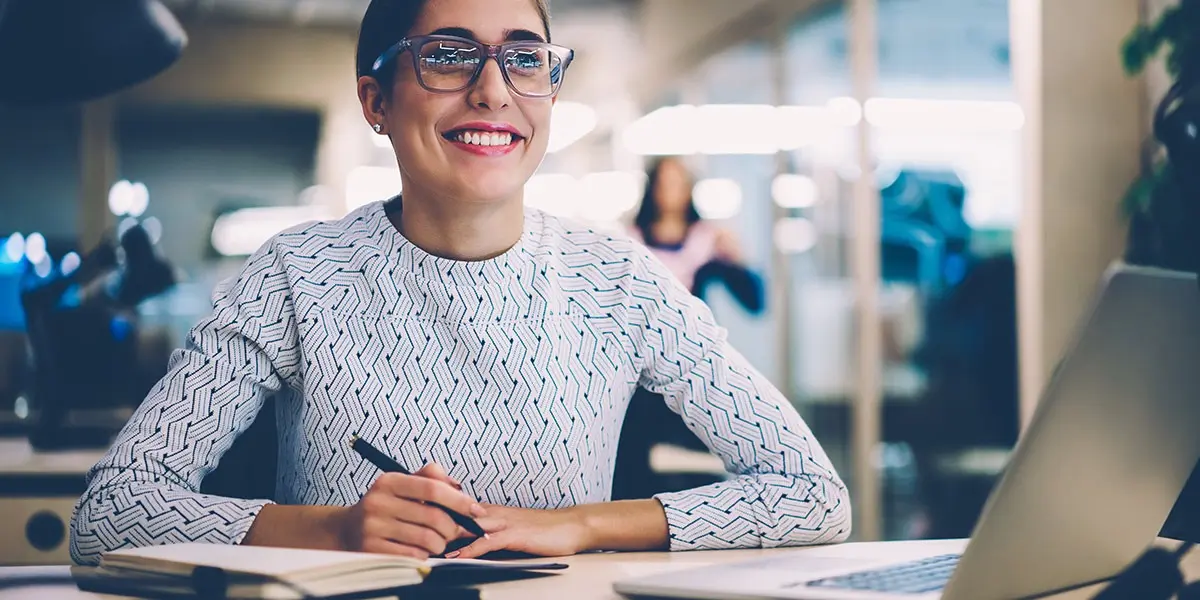 A career changer sitting at a desk with a pen and notebook, smiling