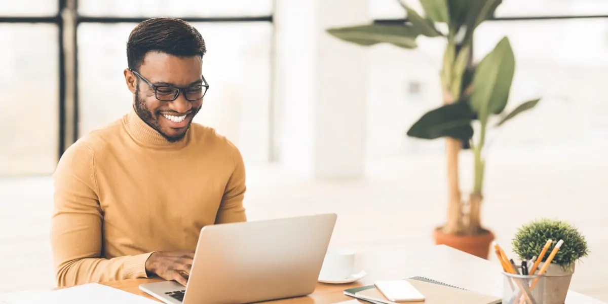 A big data engineer sitting at a desk, looking at a laptop screen, smiling, with plants in the background