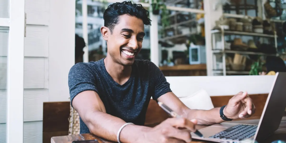 A data analyst sitting at a desk, looking at a laptop, smiling