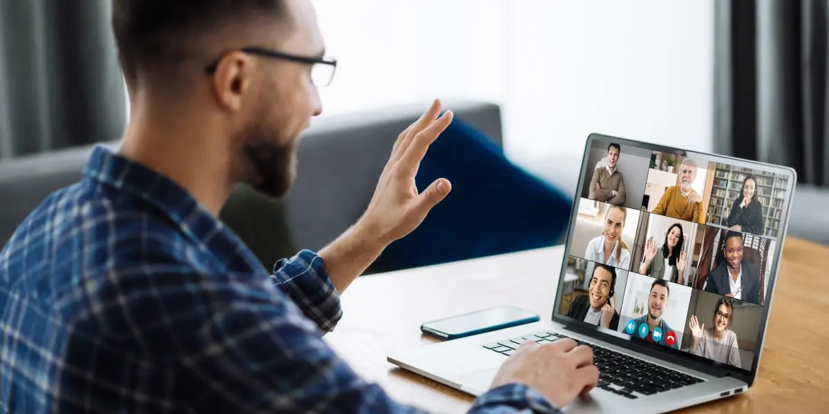 A student waves to his online coding bootcamp classmates on his laptop.