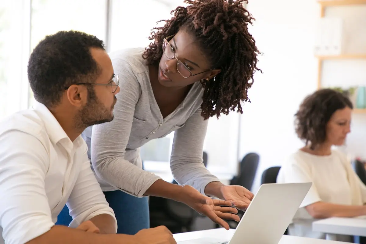 A tutor in a web development certification program helps a student at their laptop.