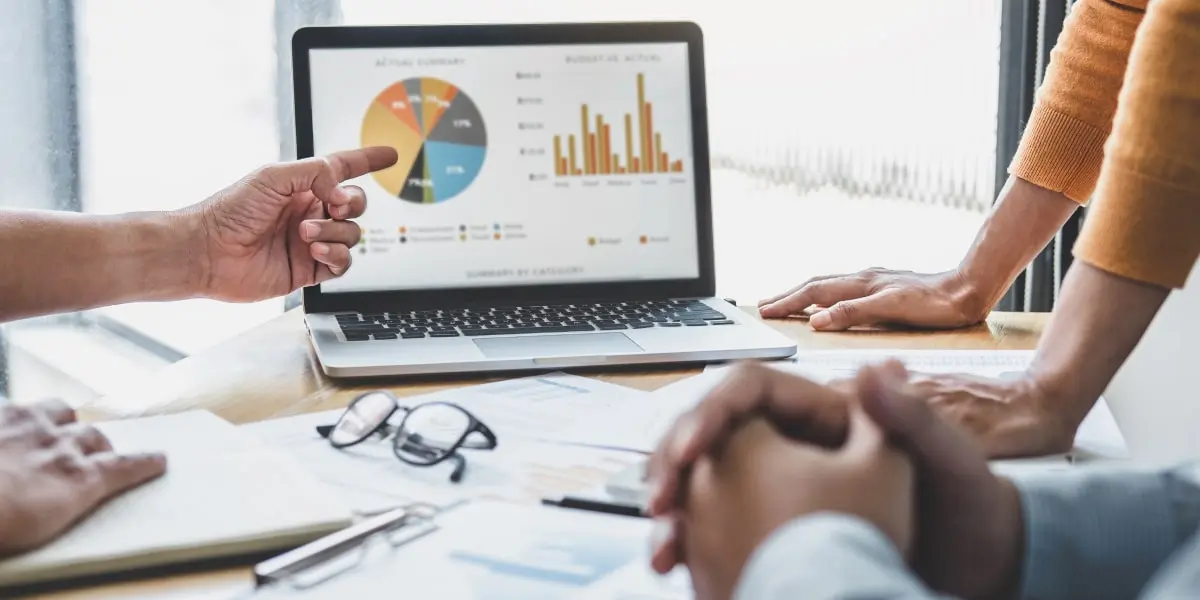 A digital marketing analyst showing graphs and data to colleagues on a laptop