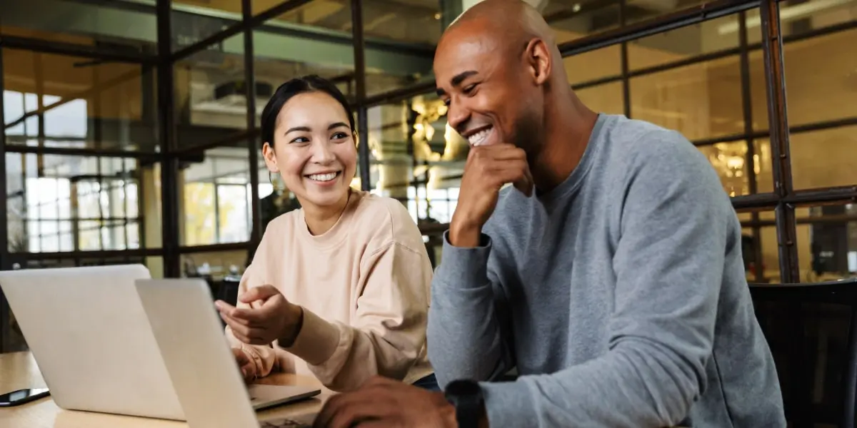 Digital marketing analyst salary worldwide Two digital marketing analysts sitting at a desk, laughing, looking at a laptop