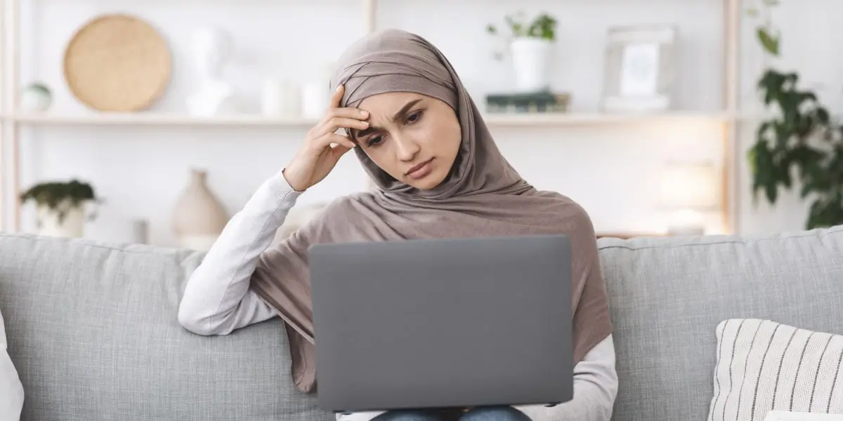 An aspiring digital marketer sitting on a sofa looking at a laptop, weighing up whether to do a digital marketing internship or a course