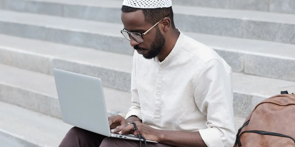 A digital marketing manager sitting on a step outside, working on a laptop