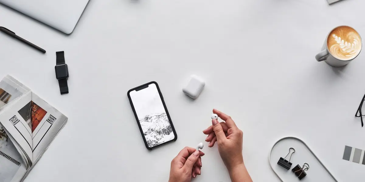 A smartphone sits on a desk beside a smartwatch, earphones, and a laptop, with an app coded with Swift on the screen.